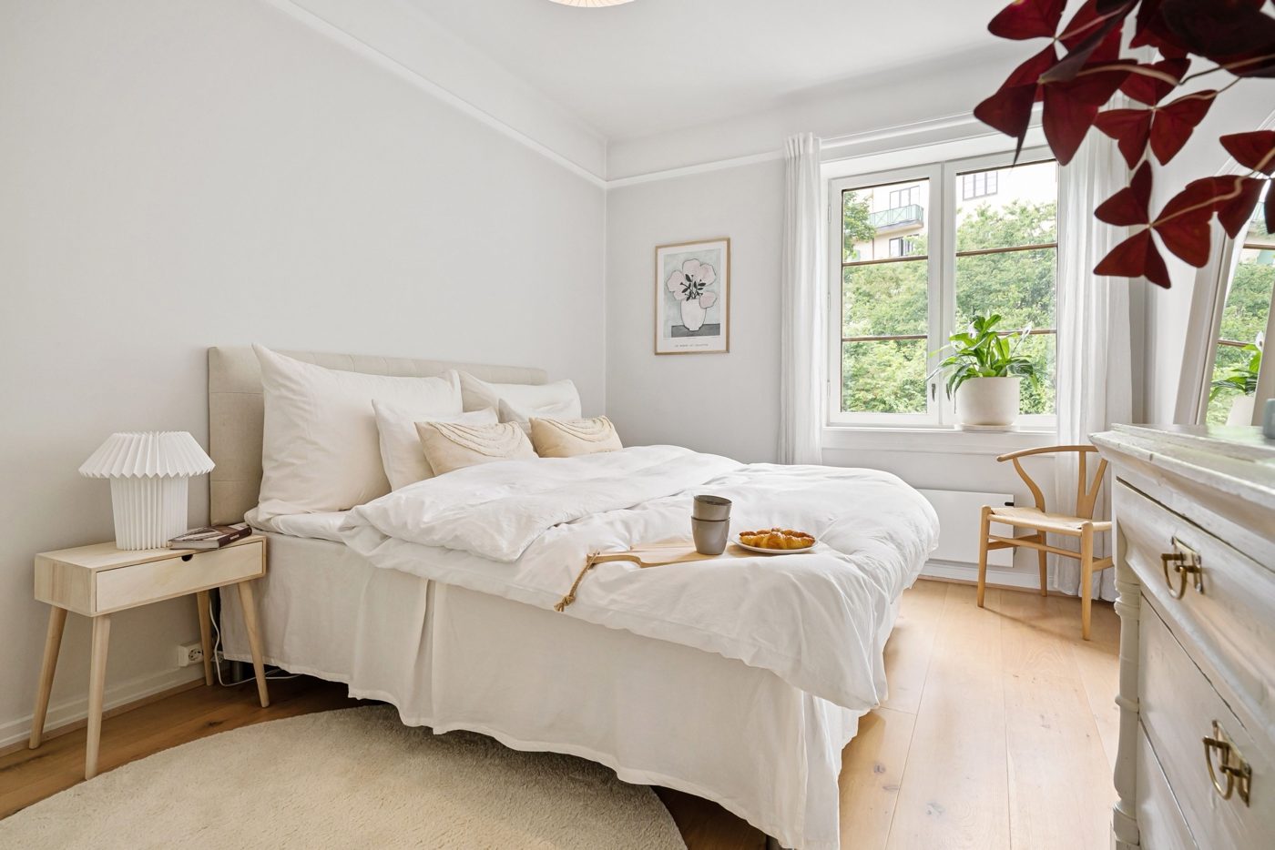 Bright bedroom with white linens and a window overlooking green trees